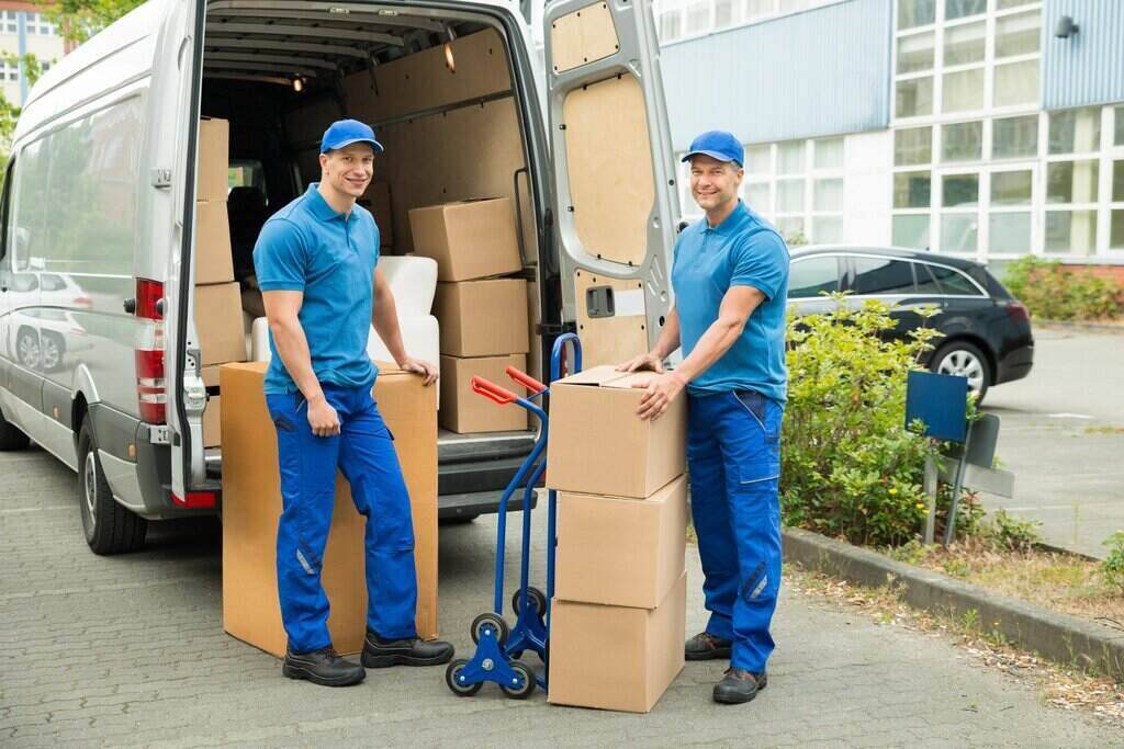 Two uniformed Go Go Agency movers with boxes and hand truck beside a moving van