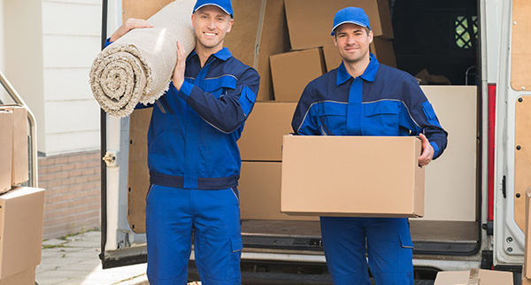 Professional movers in uniform with dolly and moving boxes